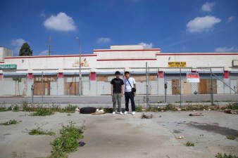 Juan Carlos Mercado and Miguel Sanchez stand in a vacant lot at Manchester and Vermont. The former swap meet site saw a groundbreaking three years ago but the mall project, planned by developer Eli Sasson, never materialized. And the buildings behind the youth - occupied by homeless folks from the area - burned down in February. Sahra Sulaiman/ Streetsblog L.A.