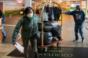 A masked woman hauls luggage in a cart at Marriot