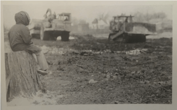 Black and white photo of a young man looking at bulldozers clearing land