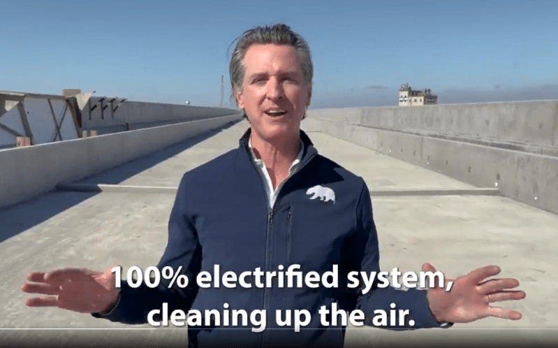 From a promotional video shot by Gavin Newsom's office. In this frame, he is standing on a bullet train viaduct in the Central Valley extolling the virtues of non-polluting, electrified trains. Image from March 2021