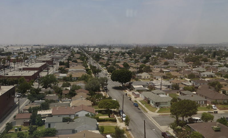 Drone shot of downtown LA skyline in the far smoggy distance, suburban city in foreground
