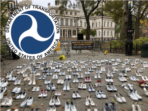 Pairs of shows arranged on a plaza; in the background a sign reads: DeBlasio, do something